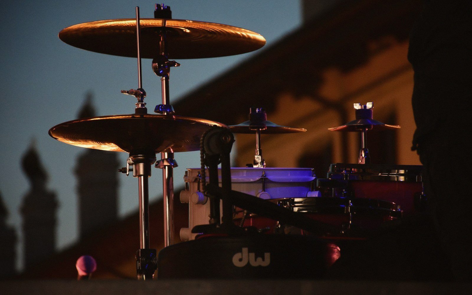 Drum kit cymbals catch sunset light against a silhouetted building skyline