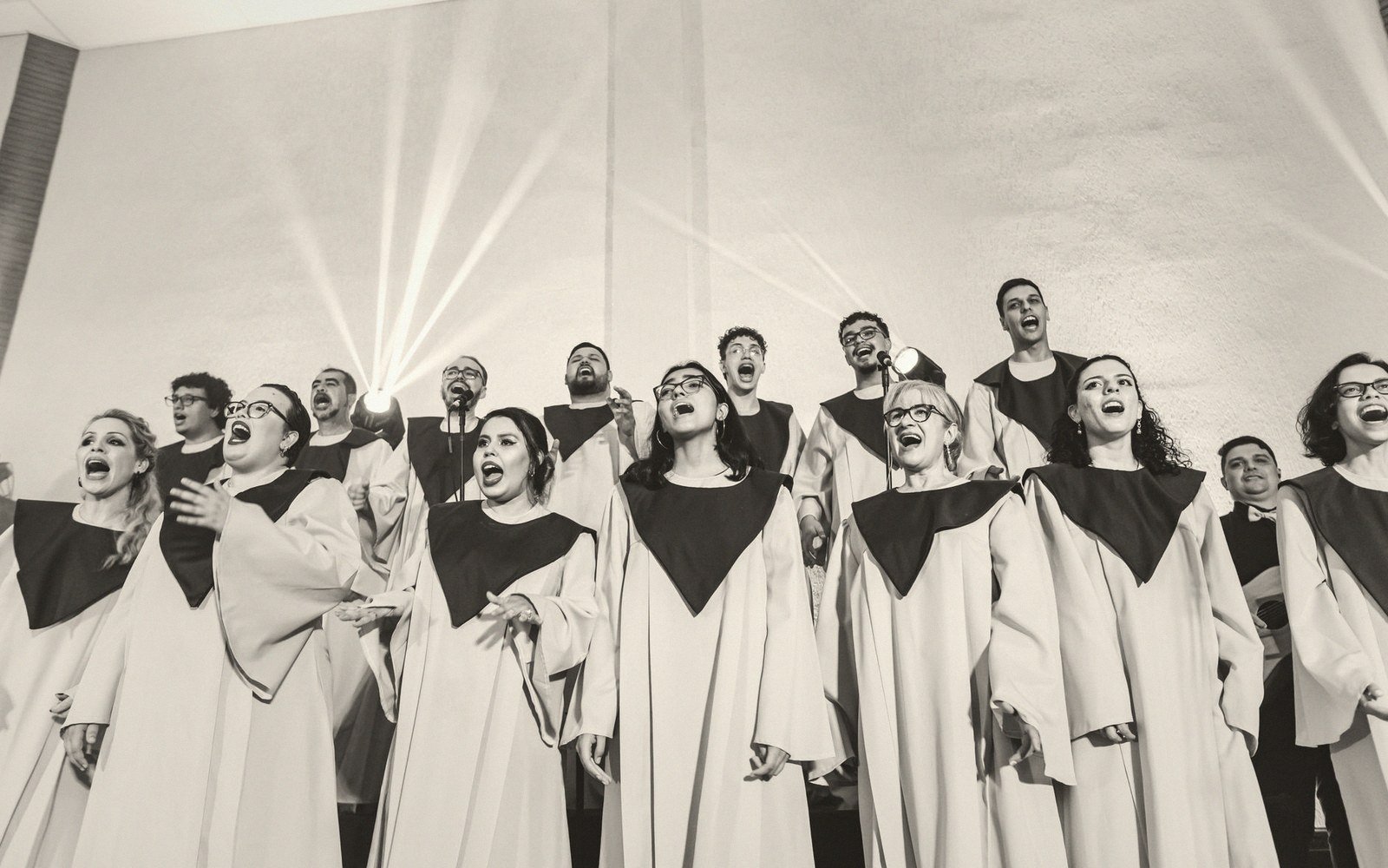 Robed choir members singing together in rows under bright stage lighting