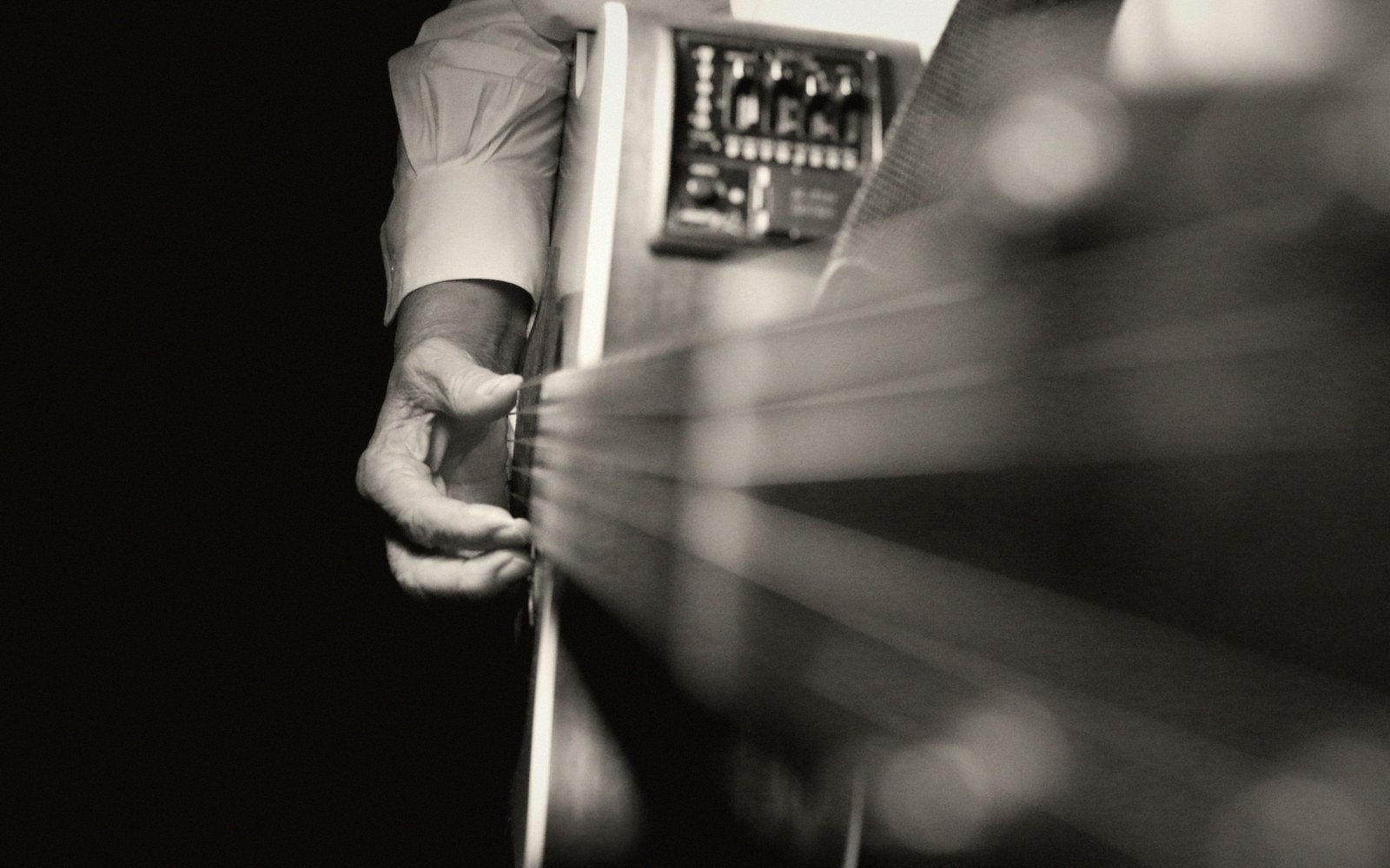 A hand frets an acoustic guitar's strings near its built-in electronic tuner
