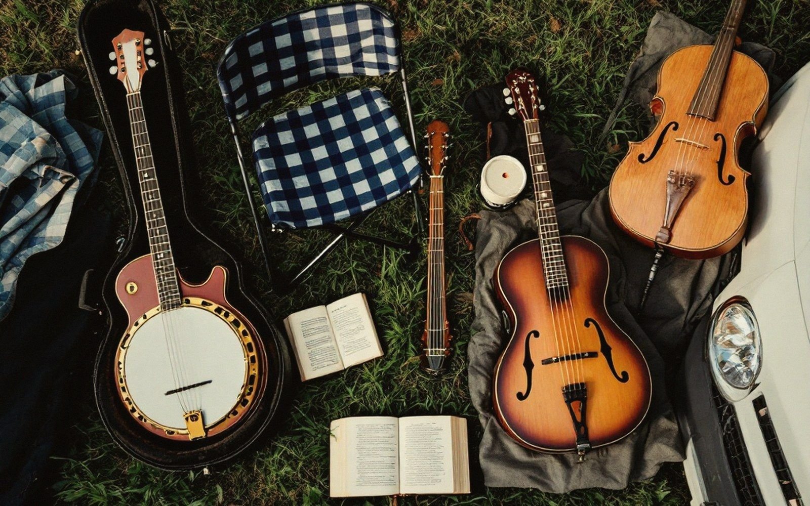 Banjo, mandolin, archtop guitar, violin and songbooks laid out on grass