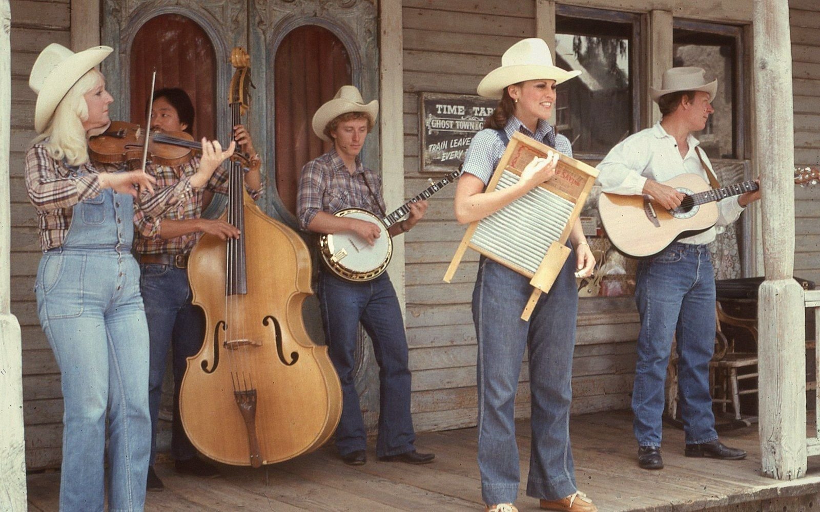 A jug band in cowboy hats plays fiddle, upright bass, banjo, washboard and guitar on a porch