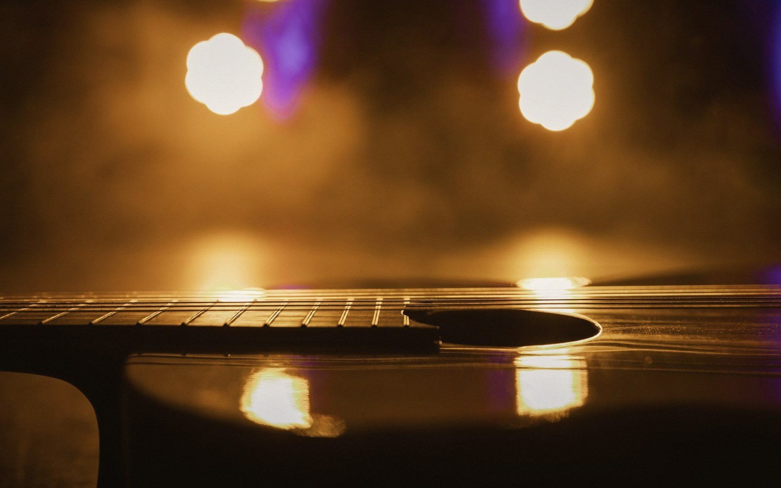 Guitar body and fretboard silhouetted against blurred stage lights on a smoky background