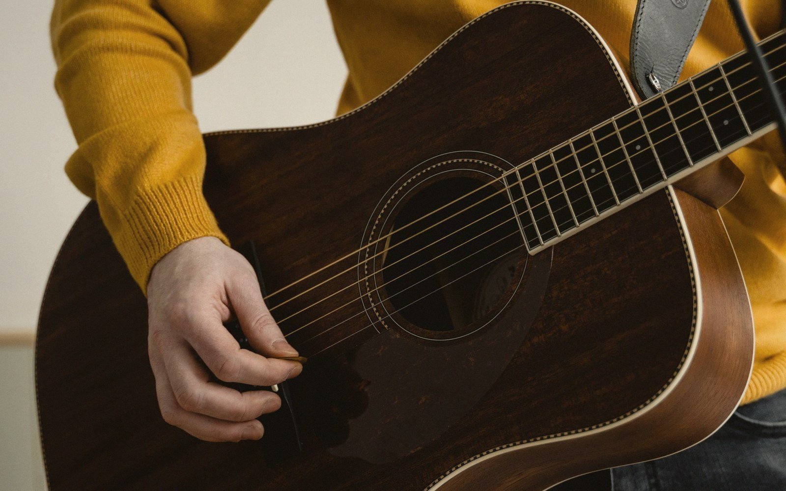 Close-up of a hand strumming an acoustic guitar with a pick